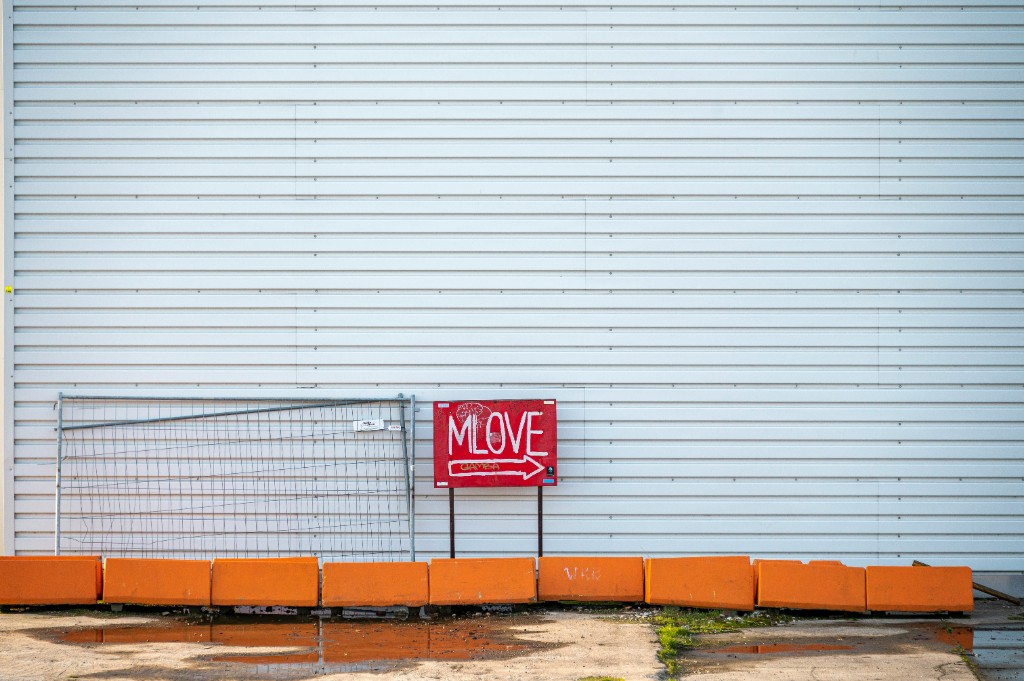A red directional sign and orange barriers against a white wall